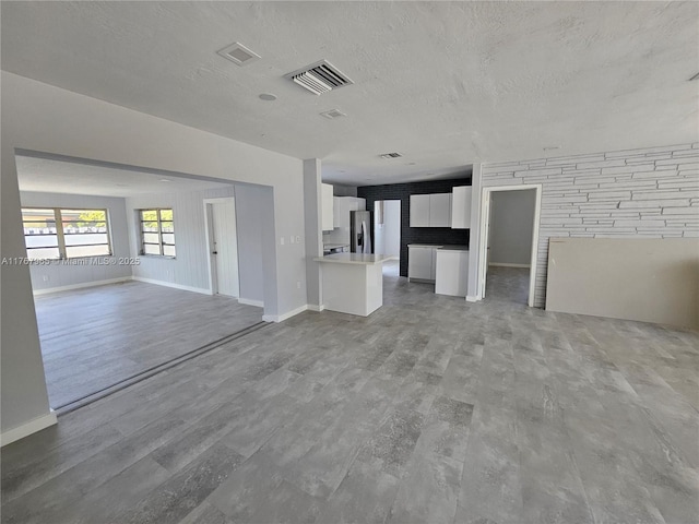unfurnished living room featuring baseboards, wood finished floors, visible vents, and a textured ceiling