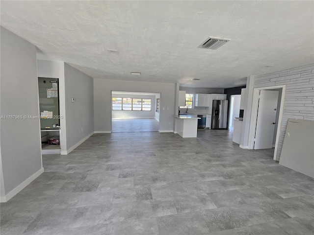 unfurnished living room with visible vents, a textured ceiling, and baseboards