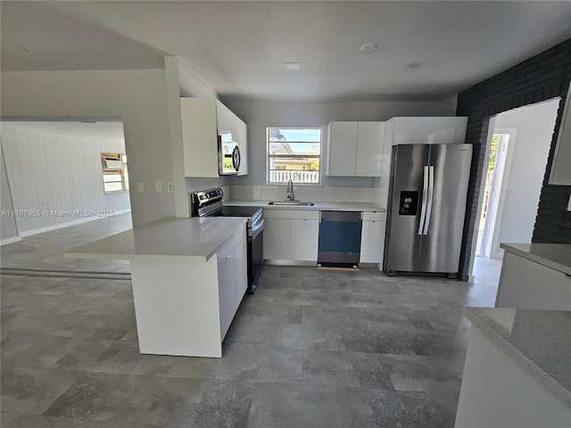 kitchen featuring a sink, stainless steel appliances, a peninsula, white cabinets, and light countertops