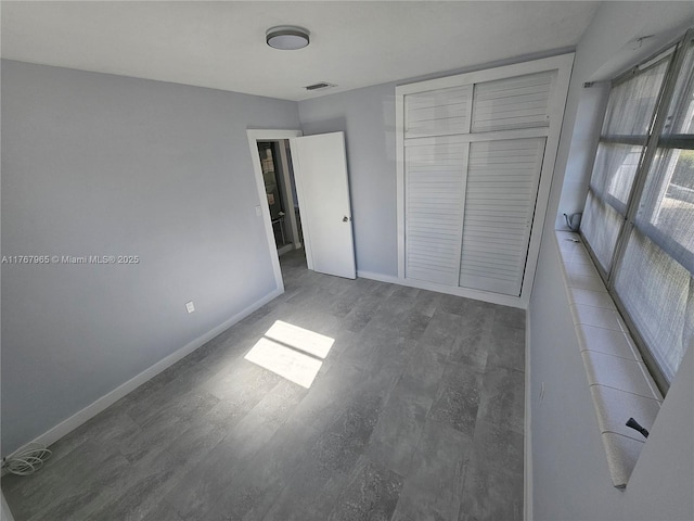 unfurnished bedroom featuring visible vents, baseboards, a closet, and wood finished floors