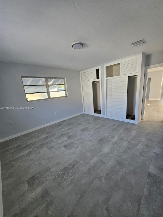 unfurnished bedroom with baseboards, visible vents, and two closets