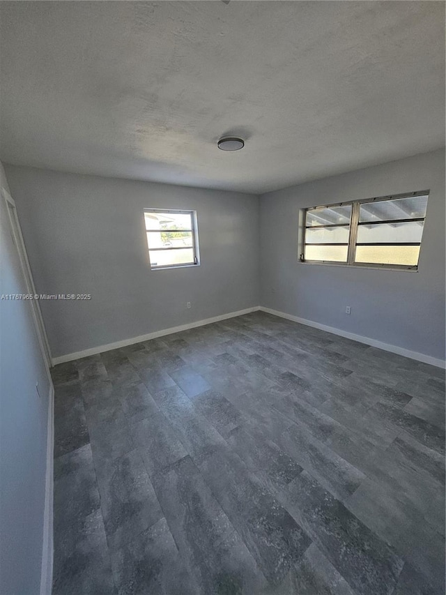 empty room featuring baseboards, dark wood-style flooring, and a textured ceiling