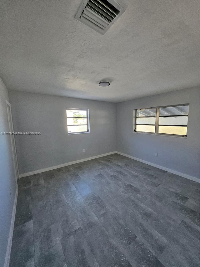 spare room featuring dark wood-style floors, visible vents, a textured ceiling, and baseboards