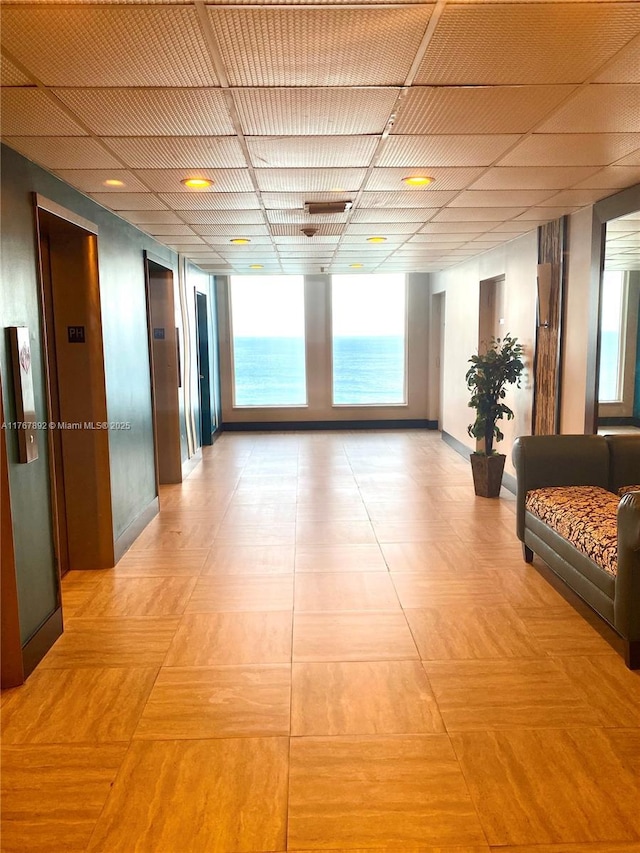 hallway featuring light tile patterned floors, baseboards, a paneled ceiling, and elevator
