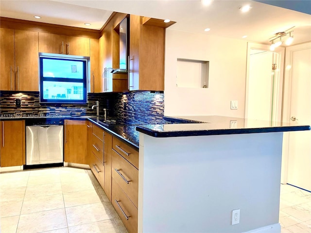 kitchen with backsplash, dark stone counters, a peninsula, brown cabinetry, and stainless steel dishwasher