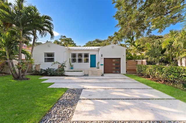 view of front facade featuring a front yard, stucco siding, metal roof, a garage, and driveway