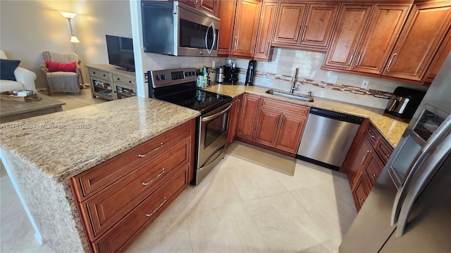 kitchen featuring light stone counters, a peninsula, a sink, appliances with stainless steel finishes, and backsplash