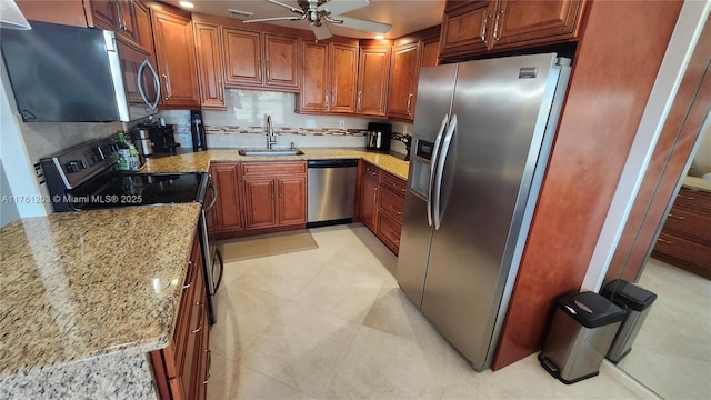 kitchen featuring tasteful backsplash, light stone counters, appliances with stainless steel finishes, a ceiling fan, and a sink