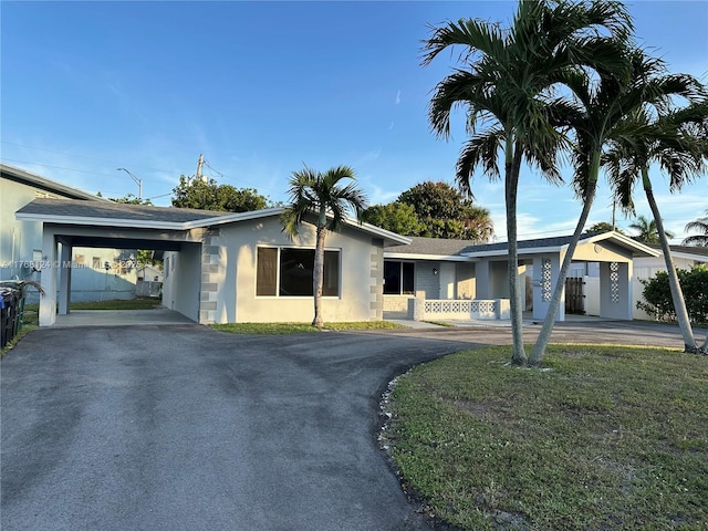 ranch-style home featuring an attached carport, a front lawn, driveway, and stucco siding