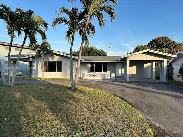 ranch-style home with an attached carport, fence, stucco siding, a front lawn, and aphalt driveway