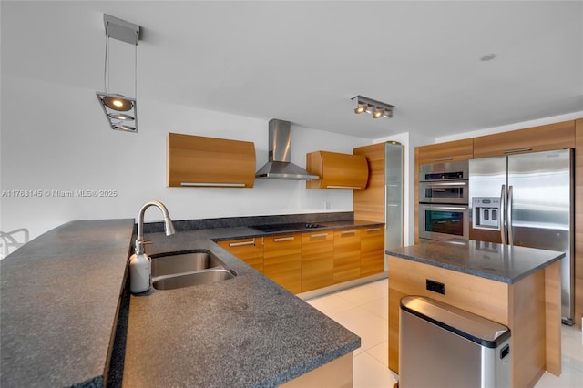 kitchen featuring stainless steel appliances, a sink, decorative light fixtures, wall chimney exhaust hood, and modern cabinets