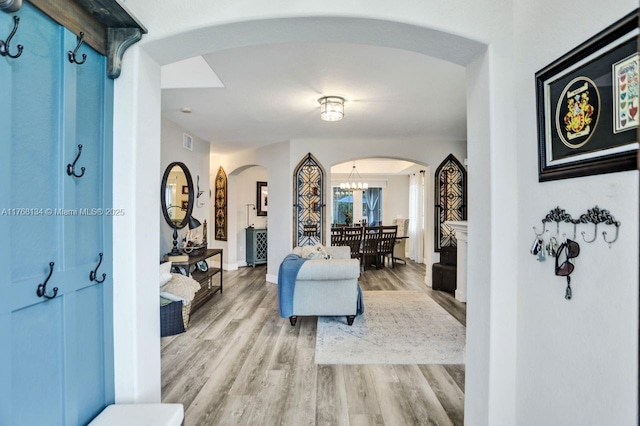 living area featuring arched walkways, visible vents, light wood finished floors, and a notable chandelier