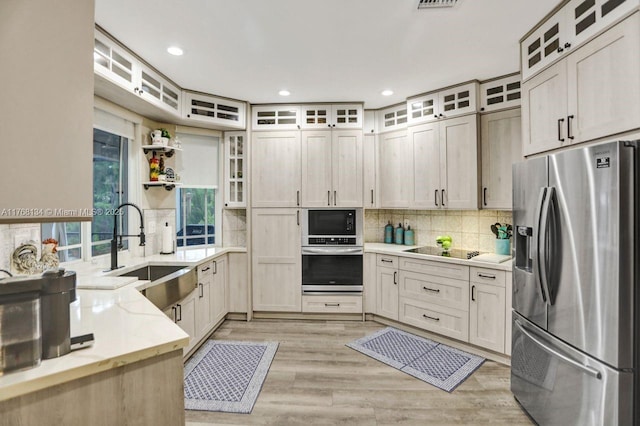 kitchen featuring light stone counters, a sink, stainless steel appliances, tasteful backsplash, and light wood-type flooring