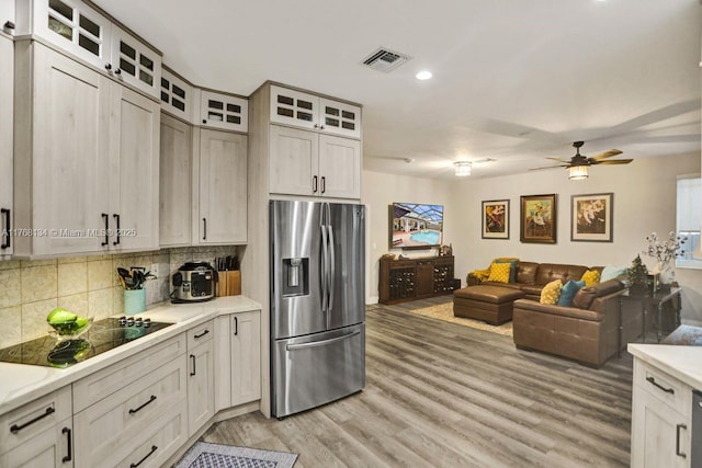 kitchen with visible vents, light wood-style flooring, stainless steel fridge with ice dispenser, light countertops, and black electric stovetop