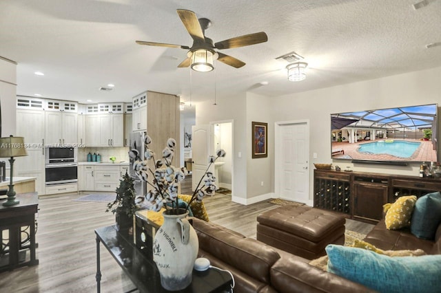 living area with a ceiling fan, baseboards, visible vents, light wood-style floors, and a textured ceiling