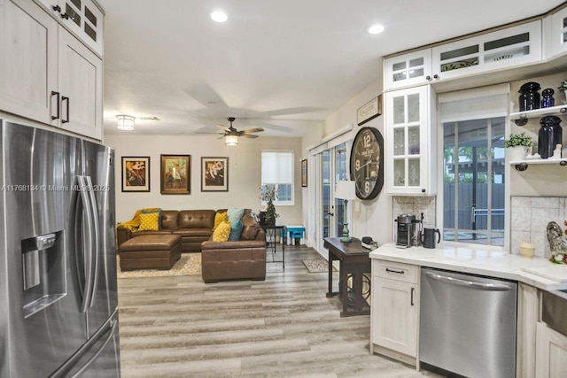kitchen featuring a ceiling fan, stainless steel appliances, white cabinets, light wood-style floors, and backsplash