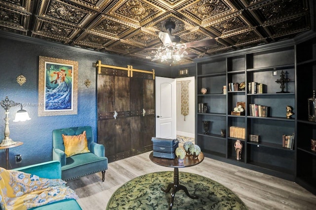 sitting room with a textured wall, an ornate ceiling, a barn door, and wood finished floors