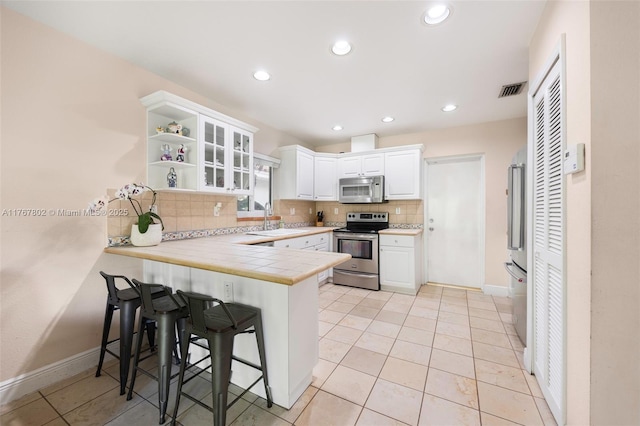 kitchen with a breakfast bar, a sink, appliances with stainless steel finishes, a peninsula, and white cabinets