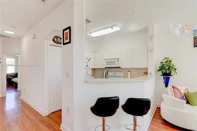 7807 NW 114th Pl, Doral, FL 33178 - kitchen featuring light wood-type flooring, visible vents, a kitchen breakfast bar, decorative backsplash, and white microwave
