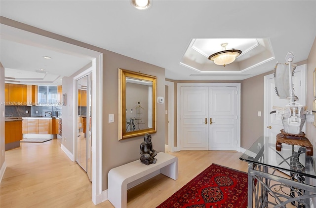 hall with a tray ceiling, recessed lighting, baseboards, and light wood-type flooring