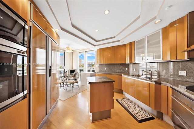 kitchen featuring decorative backsplash, light wood-type flooring, and a raised ceiling