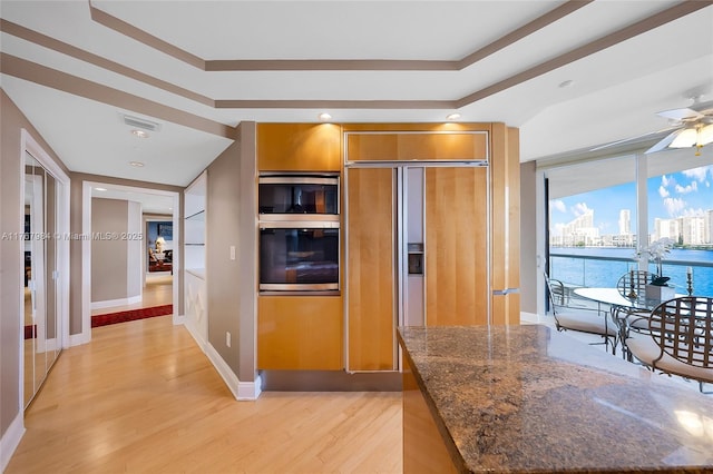 kitchen with visible vents, a city view, light wood-style floors, brown cabinetry, and stainless steel oven