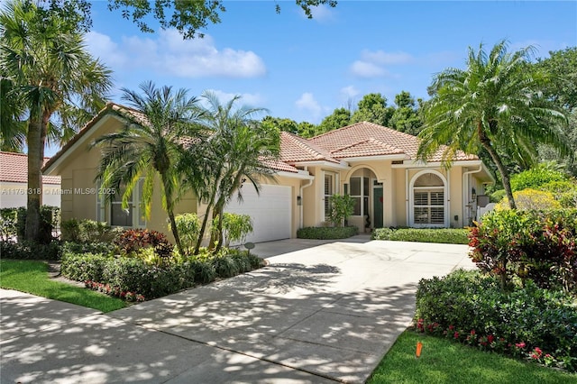 mediterranean / spanish house with stucco siding, an attached garage, concrete driveway, and a tile roof