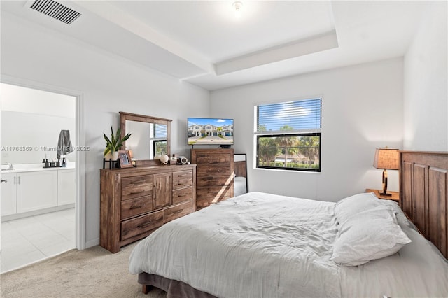 bedroom featuring a tray ceiling, visible vents, ensuite bathroom, and light carpet