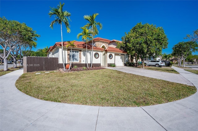 mediterranean / spanish house with concrete driveway, a tile roof, a front yard, stucco siding, and a garage