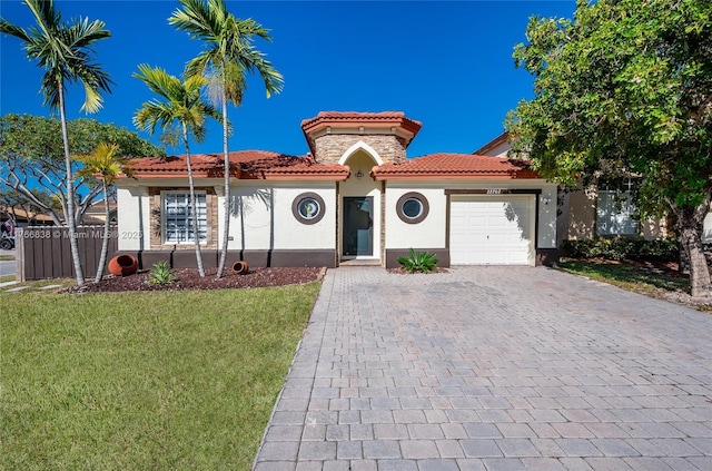 mediterranean / spanish-style house with a front yard, an attached garage, stucco siding, a tile roof, and decorative driveway