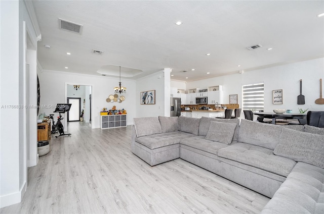 living area featuring visible vents, light wood-style flooring, and a chandelier