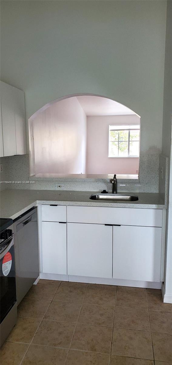 kitchen with a sink, stainless steel dishwasher, white cabinetry, light tile patterned floors, and range