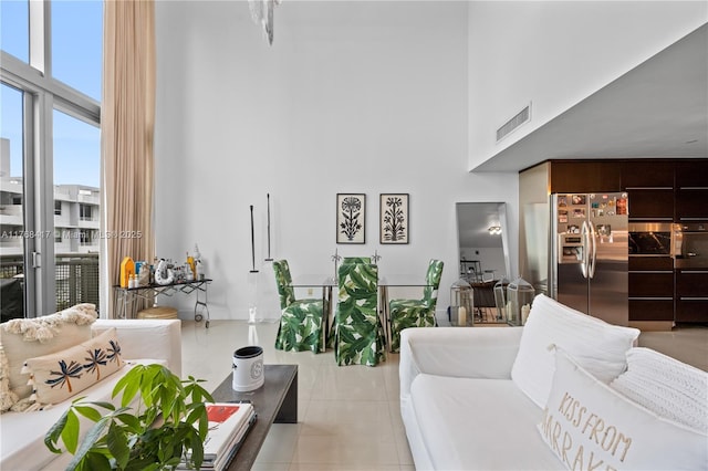 living area featuring a high ceiling, light tile patterned floors, and visible vents