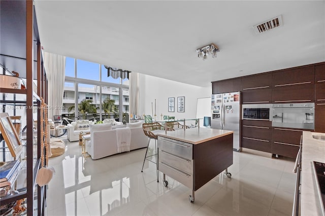 kitchen featuring light tile patterned floors, modern cabinets, dark brown cabinetry, visible vents, and appliances with stainless steel finishes