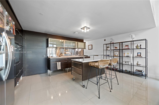 kitchen with light tile patterned floors, modern cabinets, glass insert cabinets, light countertops, and a breakfast bar area