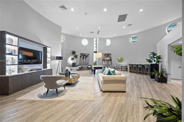 living area with visible vents, a high ceiling, and light wood-style flooring