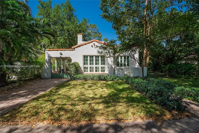 mediterranean / spanish home featuring a tile roof, stucco siding, a chimney, and a front lawn