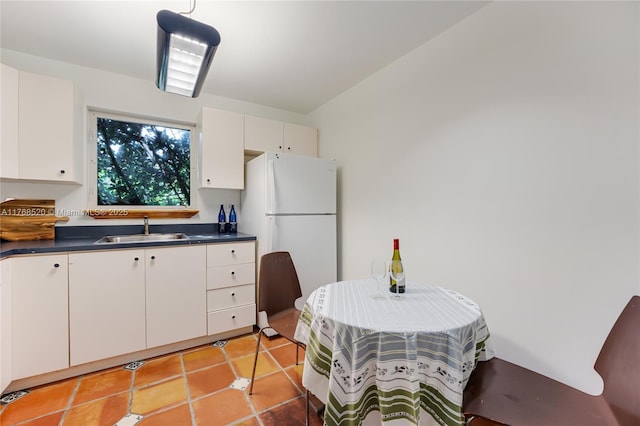 kitchen featuring light tile patterned flooring, freestanding refrigerator, a sink, white cabinets, and dark countertops