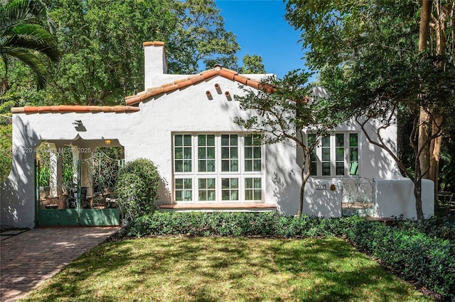 rear view of house featuring stucco siding, a yard, a tile roof, and a chimney