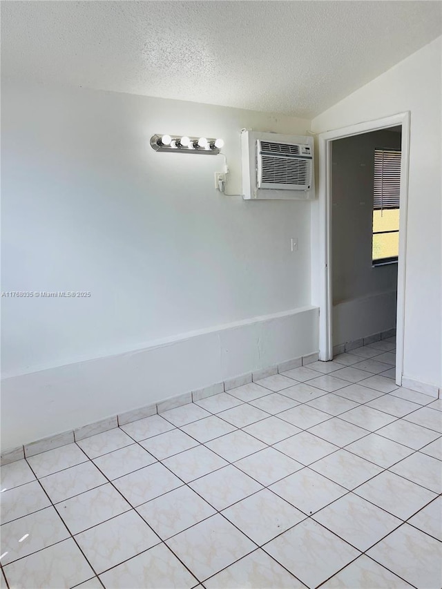 empty room with baseboards, a textured ceiling, lofted ceiling, and a wall unit AC