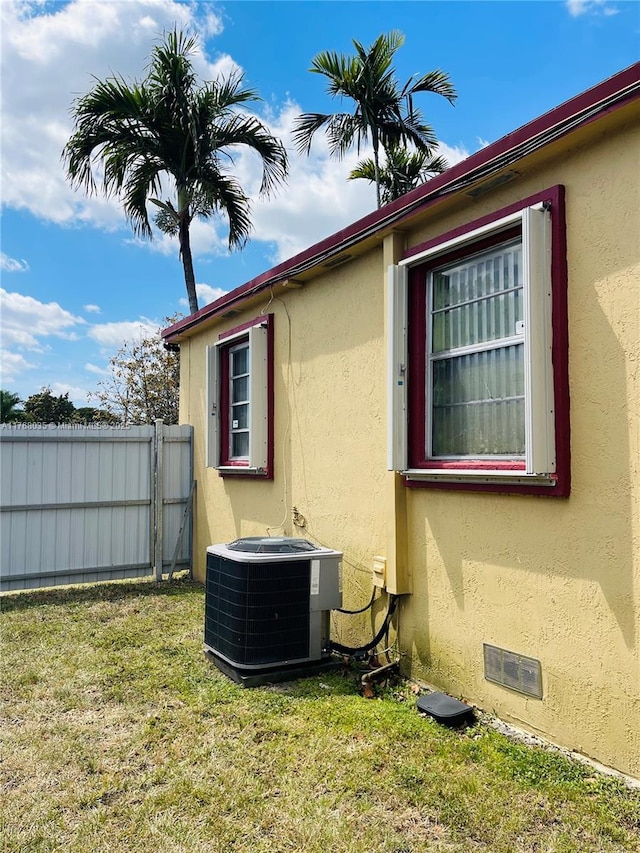 view of property exterior featuring fence, a yard, central AC, stucco siding, and crawl space