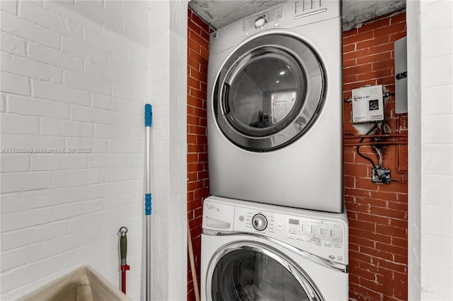 laundry area with brick wall, laundry area, and stacked washer / dryer
