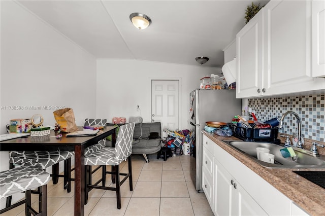 kitchen featuring backsplash, light tile patterned floors, freestanding refrigerator, white cabinets, and a sink