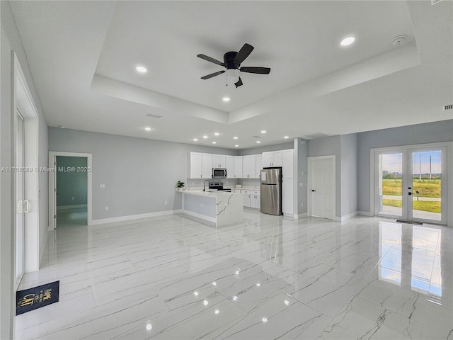 unfurnished living room featuring a tray ceiling, baseboards, a ceiling fan, and french doors
