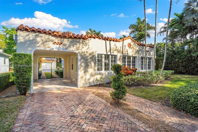 exterior space featuring a tile roof, stucco siding, an attached carport, and a gate