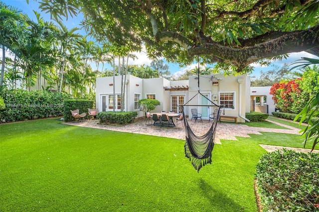 back of property featuring stucco siding, a lawn, french doors, and a patio area