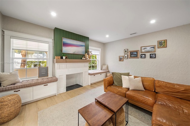 living room featuring a textured wall, a fireplace, visible vents, and light wood-type flooring