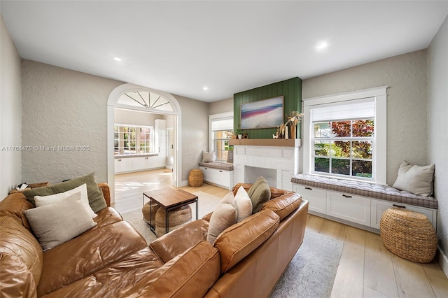 living area featuring a textured wall, recessed lighting, a brick fireplace, and light wood finished floors