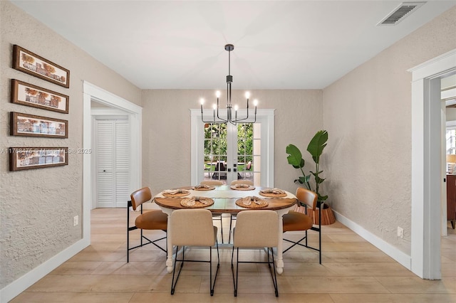 dining space featuring a notable chandelier, light wood-style flooring, baseboards, visible vents, and a textured wall