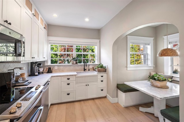 kitchen featuring a sink, white cabinetry, appliances with stainless steel finishes, light wood-style flooring, and decorative backsplash